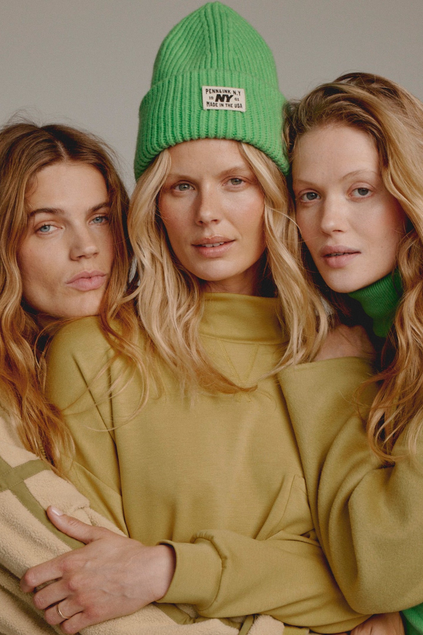 Three women wearing green and beige clothing against a neutral background